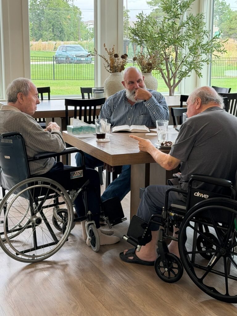 Residents sharing conversation around a table in the sunlit dining room at The Ponderosa Estate