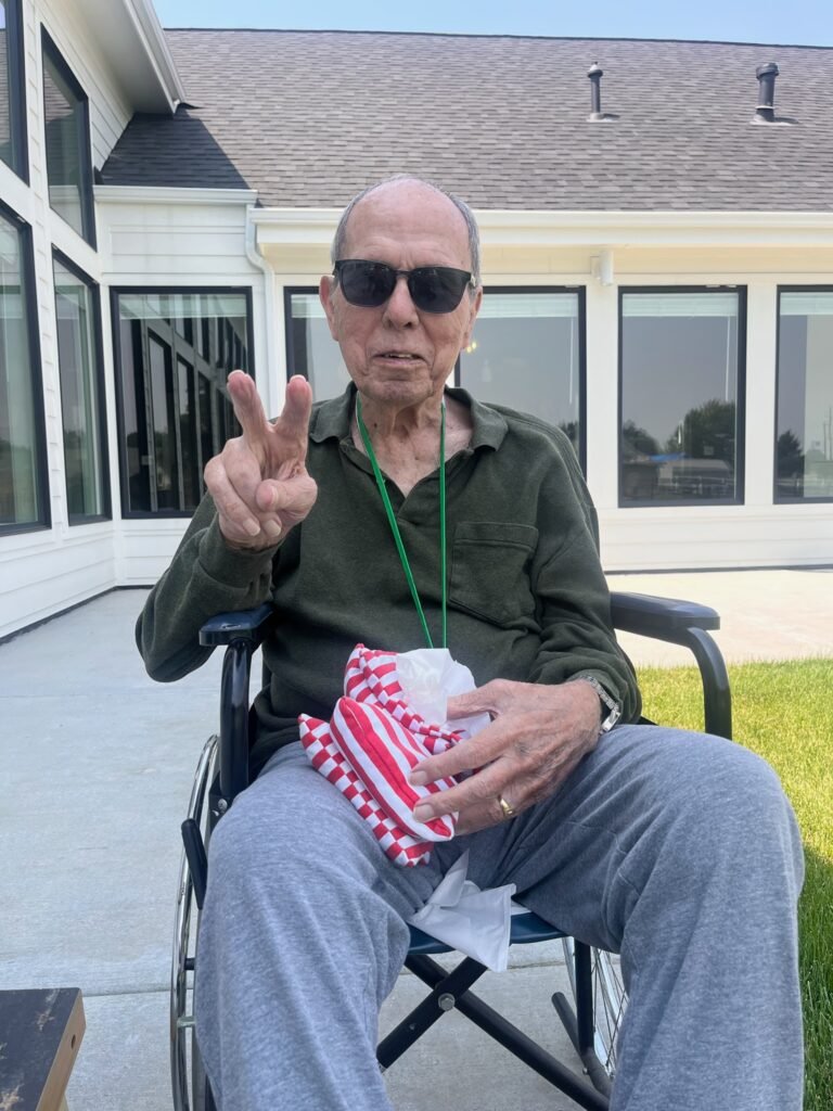 Smiling veteran resident in sunglasses giving a peace sign on the sunny patio at The Ponderosa Estate in Idaho